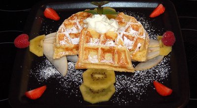A Belgian waffle topped with fresh fruit and whipped cream, elegantly presented on a black plate